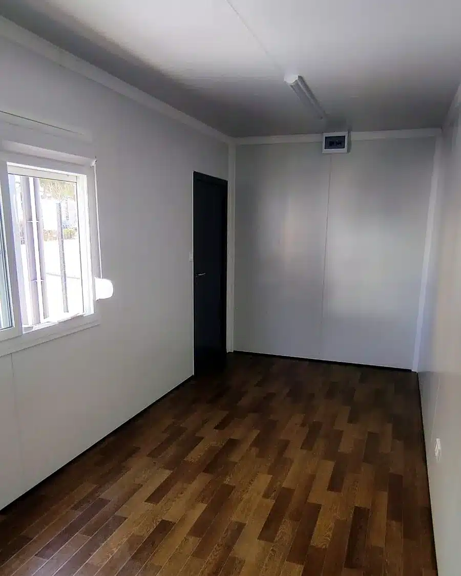 Intérieur d’un module de 6 m : parois blanches lisses, sol aspect parquet, fenêtre et tableau électrique